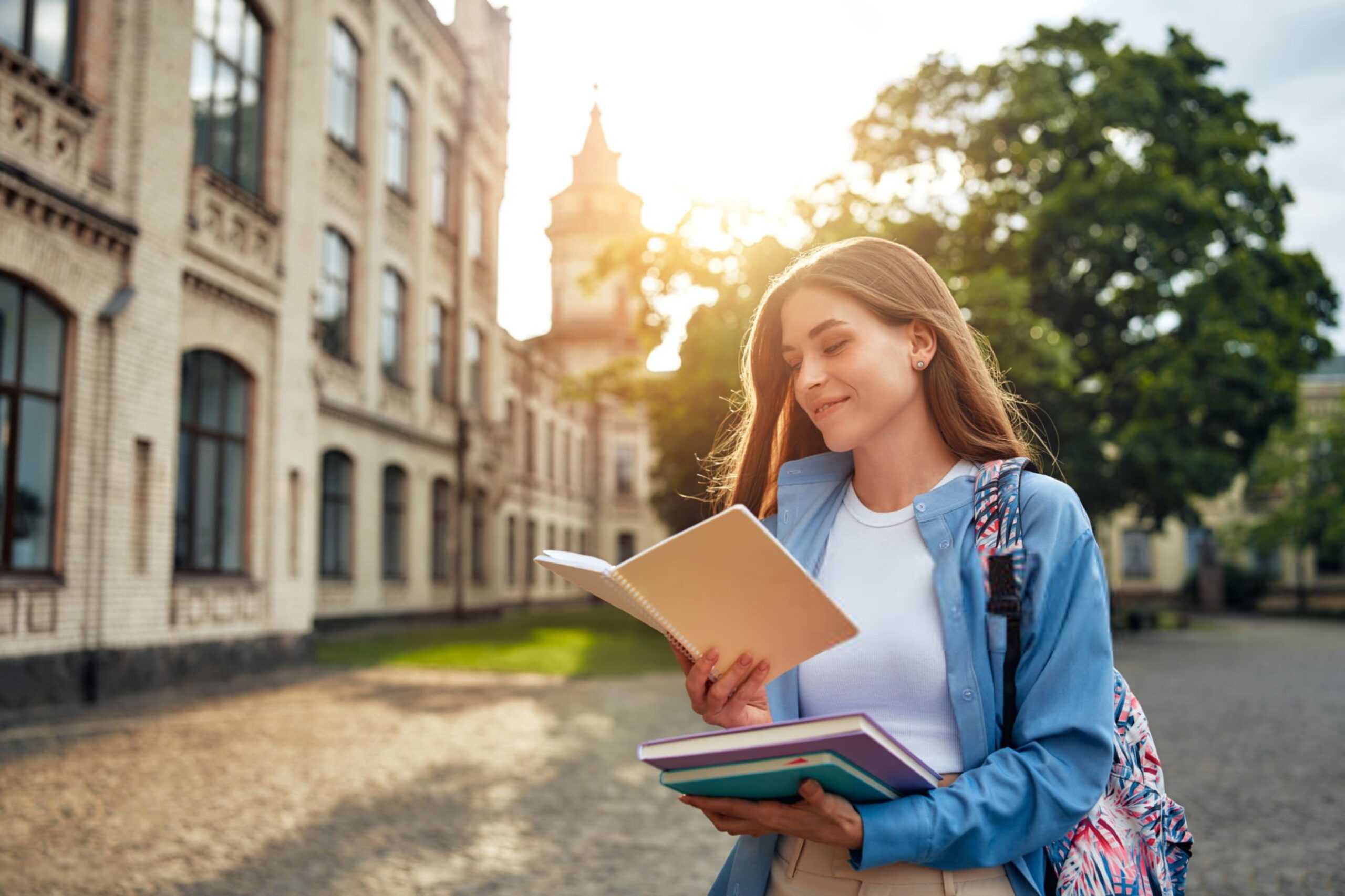 A young woman reads a book outdoors near a university at sun scaled
